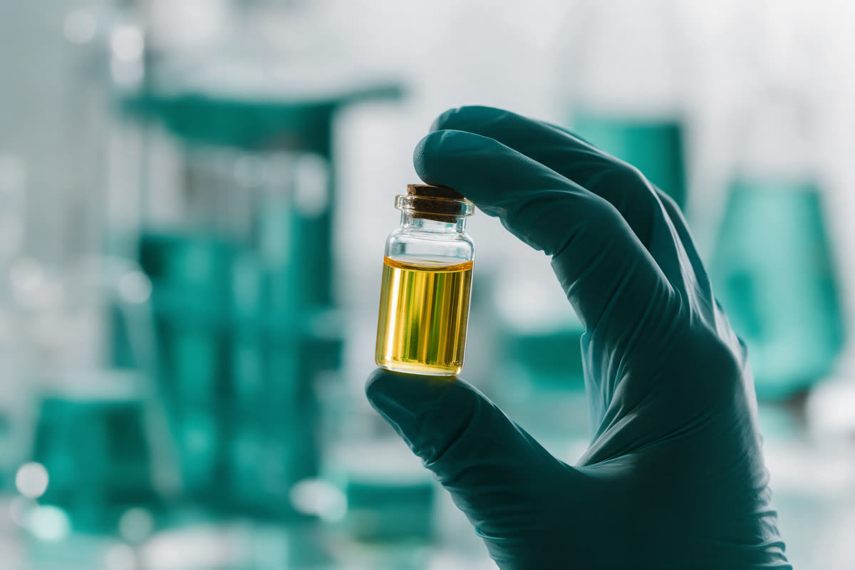 Testing an extracted oil sample Gloved hand holding a vial of clear golden oil up to the light